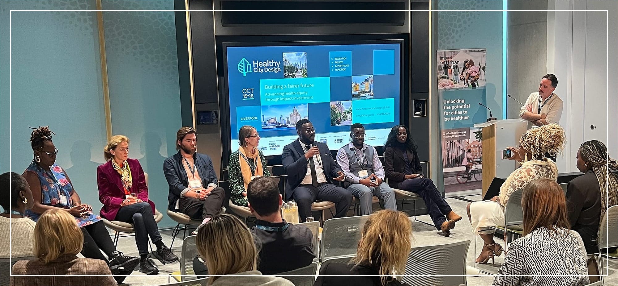 7-person panel and moderator participatory research at Healthy City Design, with speakers sharing insights and an audience listening closely.