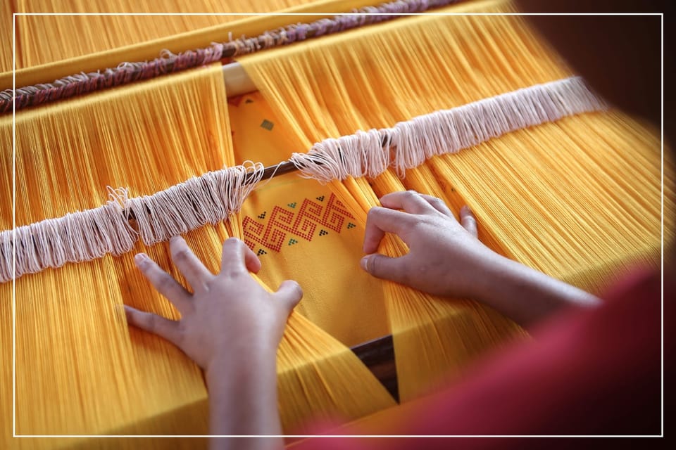 Two hands at a loom weaving a cheerful yellow Indonesian textile with red pattern.